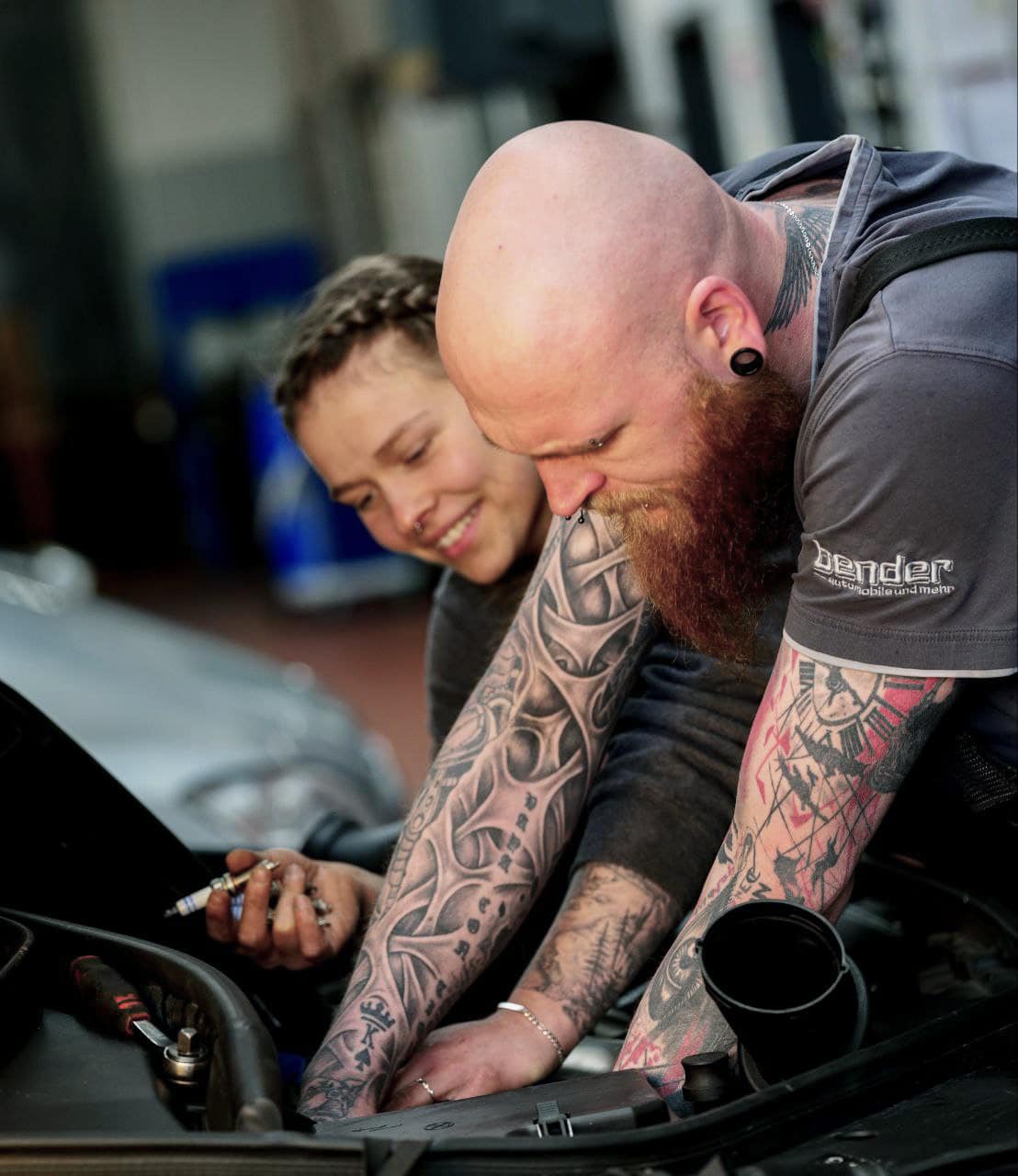 Zwei KFZ-Mechatroniker lehnen über der der offenen Motorhaube eines PKW um Wartungsarbeiten durchzuführen